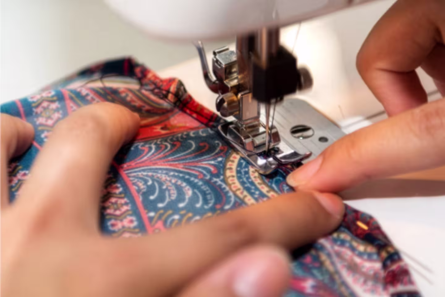 Photo rapprochée d'une machine à coudre où une personne y fait passer du matériel coloré pour en faire une couture.
