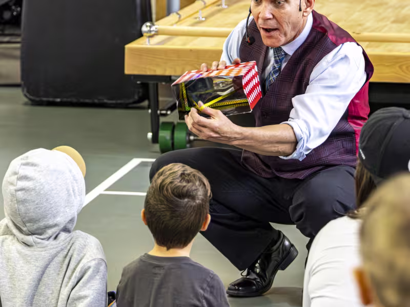 Photo du magicien René Lacourière qui montre un truc à un enfant que l'on voit de dos.