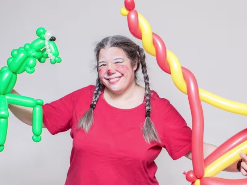 Photo de Anne Brûlé costumée en clown tenant deux sculptures de ballons.