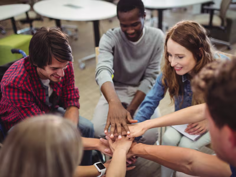 Un groupe de personnes faisant une activité d'équipe, les mains étendues vers le centre.
