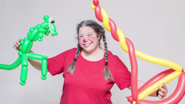 Photo de Anne Brûlé costumée en clown tenant deux sculptures de ballons.