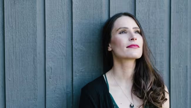 Photo de Kristine St-Pierre, pensive, devant un mur gris-bleu foncé.